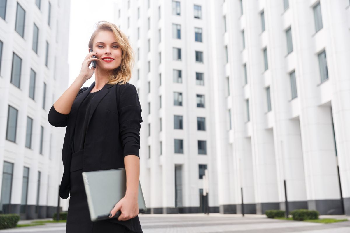 Attractive blonde businesswoman with phone and laptop on urban backgroud